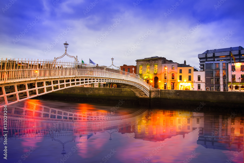Obraz premium Most Ha'penny na rzece Liffey w Dublinie w Irlandii wieczorem ze światłami i refleksami
