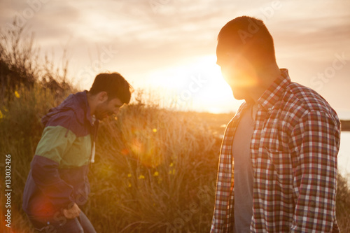 Two friends on water's edge talking at sunset