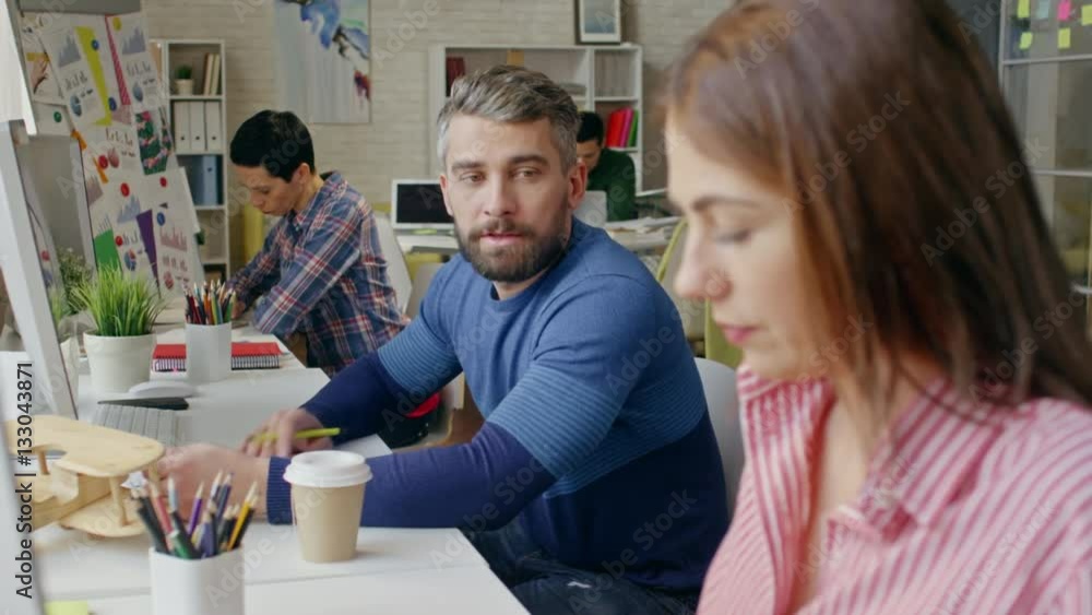 Tilt down with rack focus of young businesswoman in casual clothing typing on computer and chatting with bearded colleague at work Tilt down with rack focus of young businesswoman in casual clothing typing on computer and chatting with bearded colleague at work