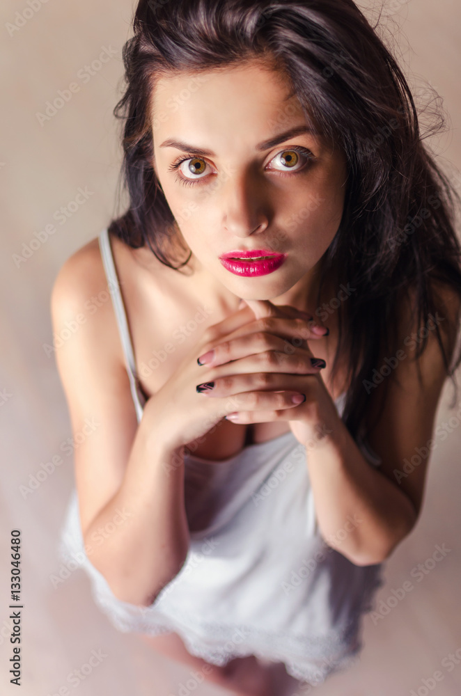 Seductive and tender model looks up to the camera. Portrait of woman in gentle nightgown in pastel colors. Seductive and tender model looks up to the camera. Portrait of woman in gentle nightgown in pastel colors.