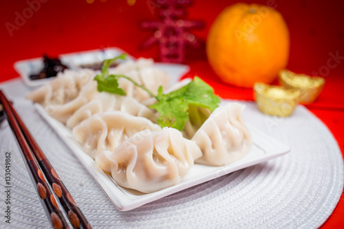 Chinese Jiaozi new year food with sauce and white placemat on red background. People will eat Jiaozi during Chinese New Year.It means earning more money.The Chinese text is 