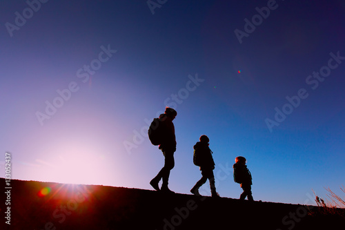 Silhouettes of mother and two kids hiking at sunset