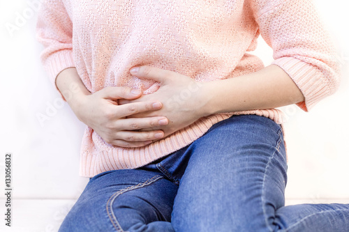 Young woman with stomach issues. woman white sport shirt stomachache and hand at abdomen. menstruation pain or stomach ache, hand holding belly closeup