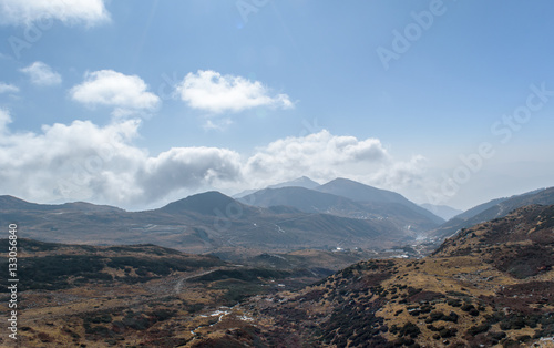 A hilltop view of mountains and blue sky with clouds.