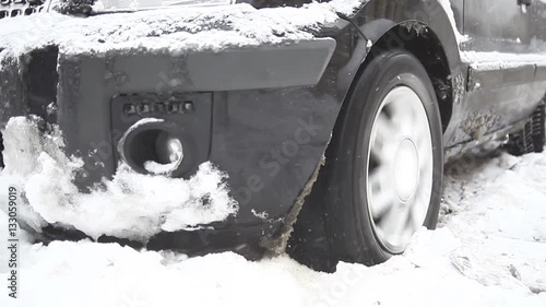 Color footage of a car's wheel being stuck in snow, and spinning.