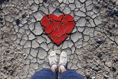 Foto Lonely man standing on dried soil ground with illustrated cracked heart symbol