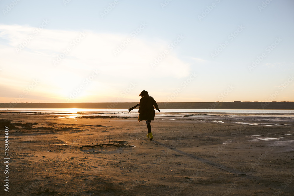 Beautiful girl is standing near sea on winter and see to the sundown, black coat, beautiful eyes, model, a beautiful sunset, the sun's rays, reflection in water Beautiful girl is standing near sea on winter and see to the sundown, black coat, beautiful eyes, model, a beautiful sunset, the sun's rays, reflection in water