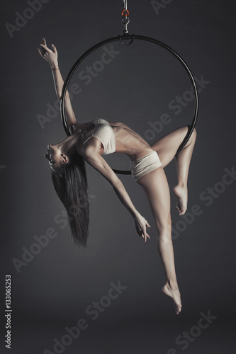 Young beautiful slim dancer on aerial hoop posing on a black studio background.
