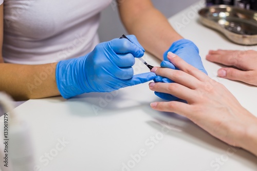 Professional beautician applying nail polish to female nail