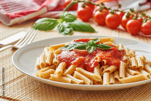 Pasta with tomato sauce and basil on white dish, vegetable in the background