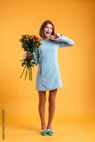 Happy surprised young woman standing and holding bunch of roses