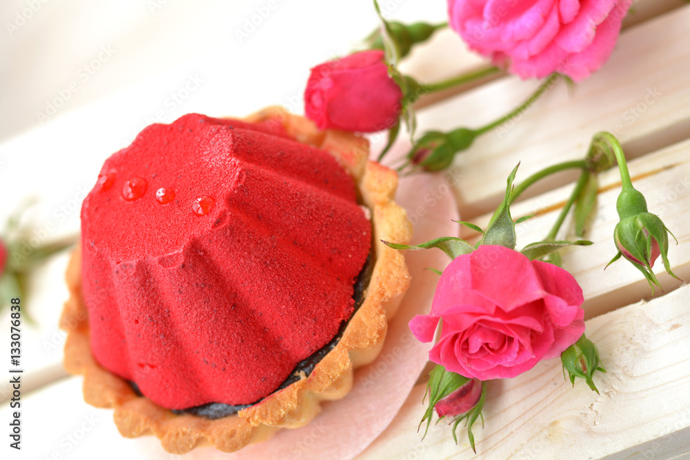 Sweet and red cake full of chocolate near pink rose on light brown, wooden background close up Sweet and red cake full of chocolate near pink rose on light brown, wooden background close up