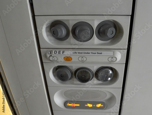 Individual lighting and fans are mounted in panel above passenger seats in cabin. Illuminated display "No Smoking. Fasten seat belts". Closeup