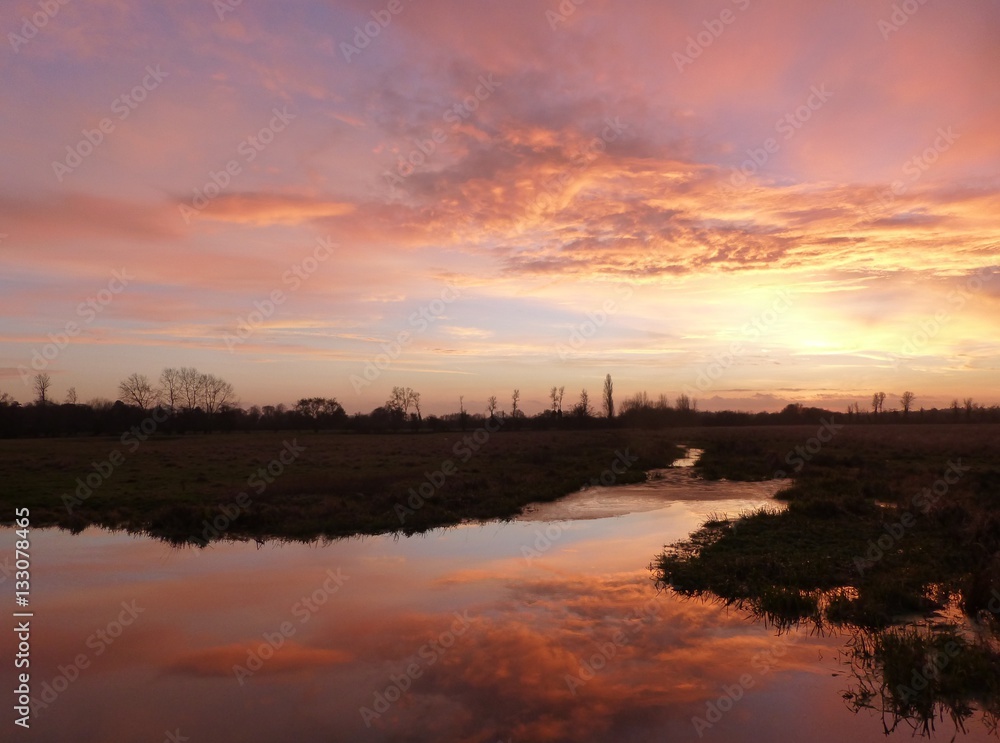 Dramatic sunset over the Widbrook stream near Cookham, Berkshire, with clouds reflected in the calm waters of the stream