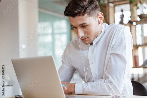 Serious man using laptop while listening music.