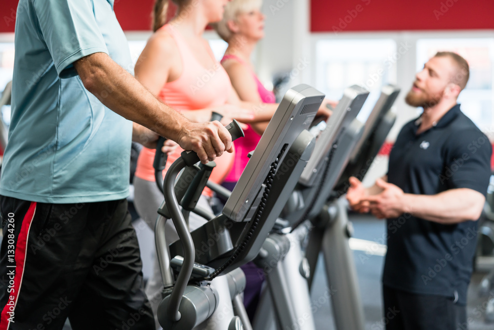 Seniors training on cross trainer with personal trainer at the g Seniors training on cross trainer with personal trainer at the g