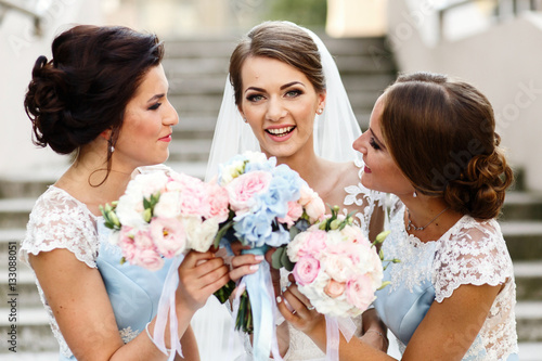 Bridesmaids look at smiling bride holding wedding boquuets behin