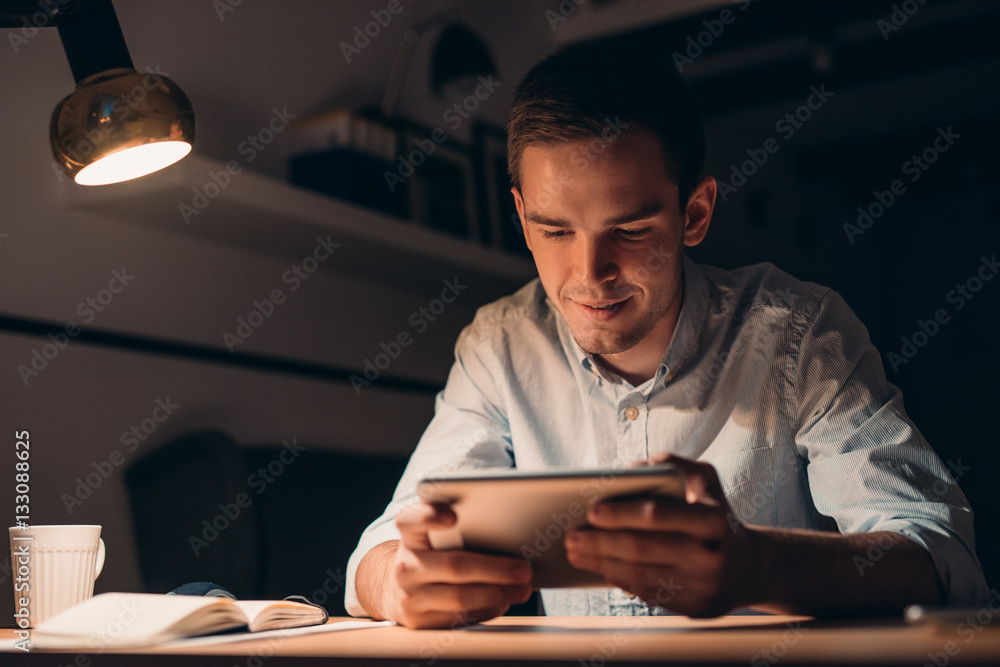 Fototapeta premium Young businessman working using a tablet late at night