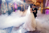Groom holds bride's hands tender while they dance in the smoke