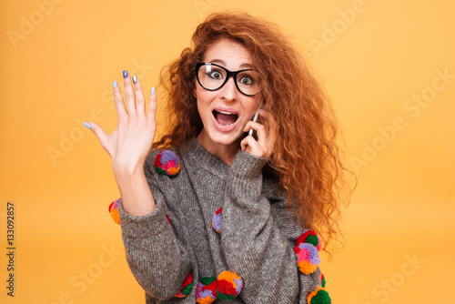 Young astonished woman with red hair talking on mobile phone photo