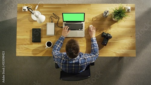 Top View of a Young Photographer Processing Photograps on His Laptop With Green Screen. Camera, External Hard Drive and Notebook Lie Beside Him.  Shot on RED Cinema Camera in 4K (UHD). photo