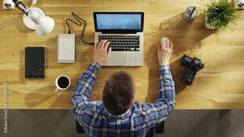  Top View of a Young Photographer Processing Photograps on His Laptop. Camera, External Hard Drive and Notebook Lie Beside Him. Shot on RED Cinema Camera in 4K (UHD). photo