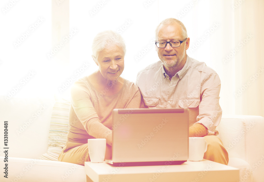 happy senior couple with laptop and cups at home