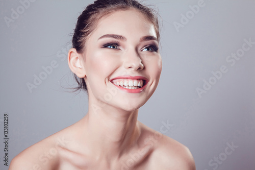 Smiling brunette girl with beautiful makeup on grey background, youth and skin care concept.