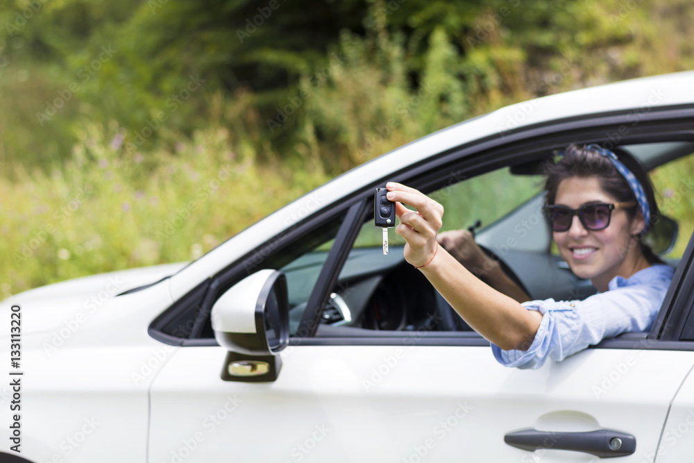 Young happy woman driving new white car with keys in the hand