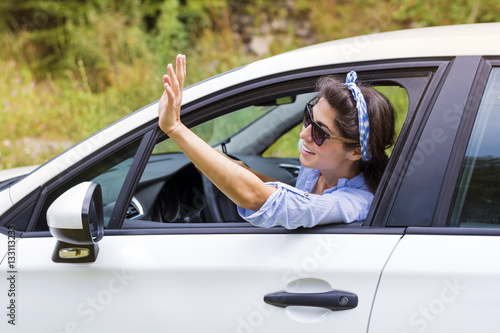 Young happy woman driving new white car and waving 