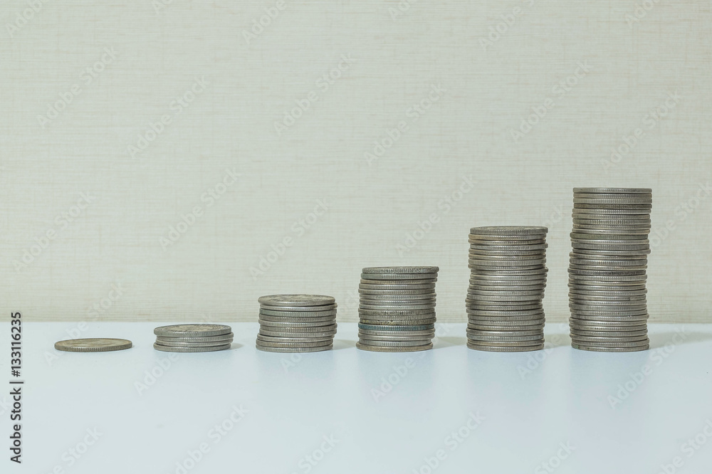 Closeup pile of coin start from low to high on white wood desk and cream wallpaper textured background with copy space Closeup pile of coin start from low to high on white wood desk and cream wallpaper textured background with copy space