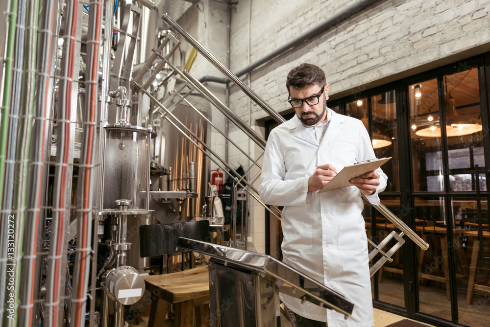 Serious man noting results at beer factory Serious man noting results at beer factory
