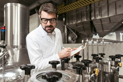 Concentrated man noting work results on beer factory