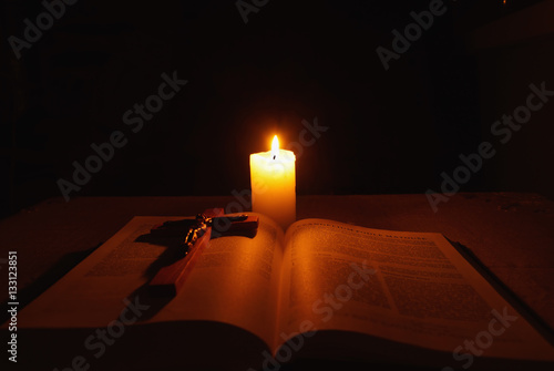Burning candle, bible and crucifix on desk