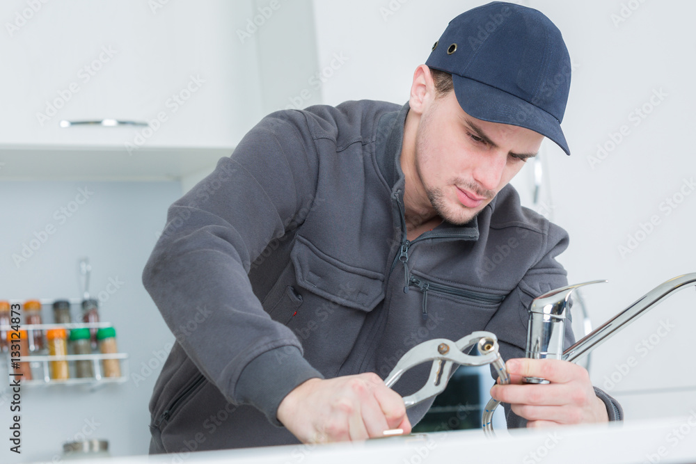 handsome young plumber fixing tap at cleints home
