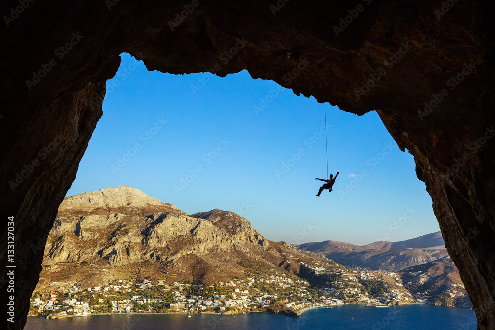 Silhouette of a rock climber hanging on rope while climbing in cave, Telendos Island, Greece