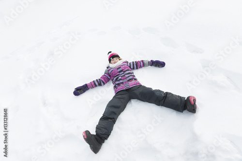 Little girl in winter pink hat in snow forest doing an angel