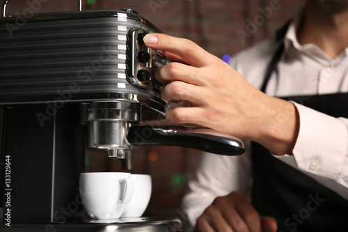 Male barista making fresh espresso in coffee maker, close up