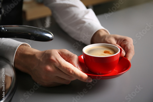 Male barista holding red cup of coffee at table