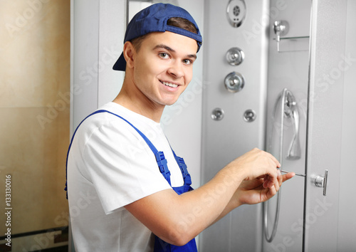 Young plumber fixing shower cabin
