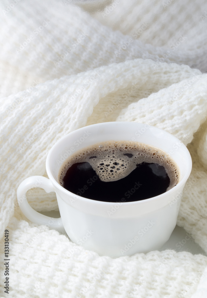 White cup with hot coffee wrapped in a white woolen scarf White cup with hot coffee wrapped in a white woolen scarf