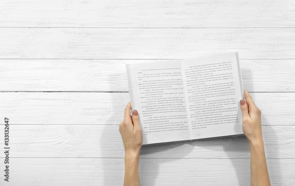Obraz premium Female hands holding opened book on wooden background