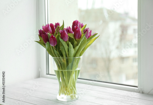 Glass vase with bouquet of beautiful tulips on windowsill