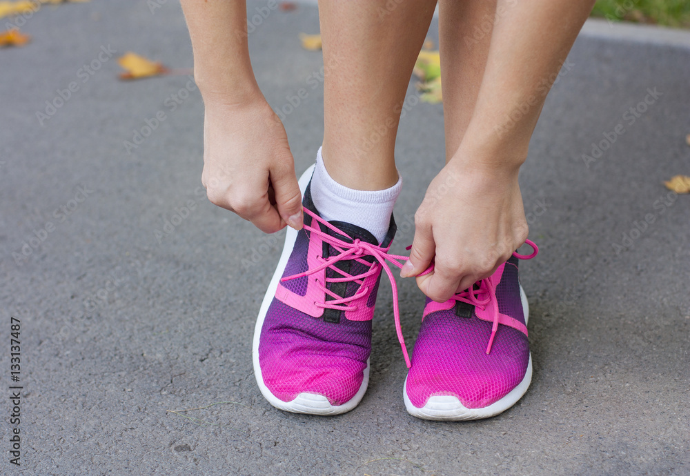 Woman tying shoelace on running shoes before practice. Bright  running  shoes. Fitness woman in training shoes jogging outdoors in park. 
