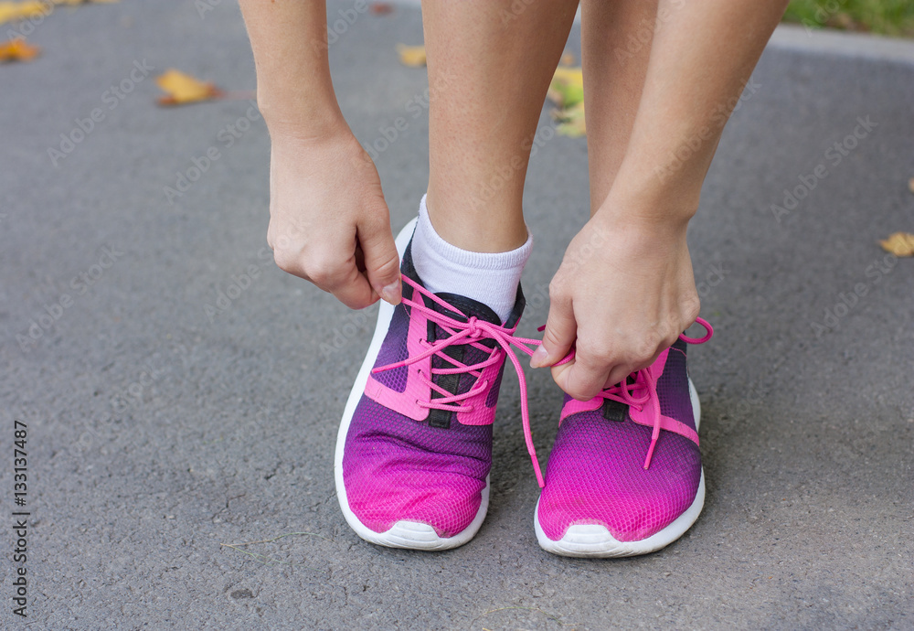 Naklejka premium Woman tying shoelace on running shoes before practice. Bright running shoes. Fitness woman in training shoes jogging outdoors in park.