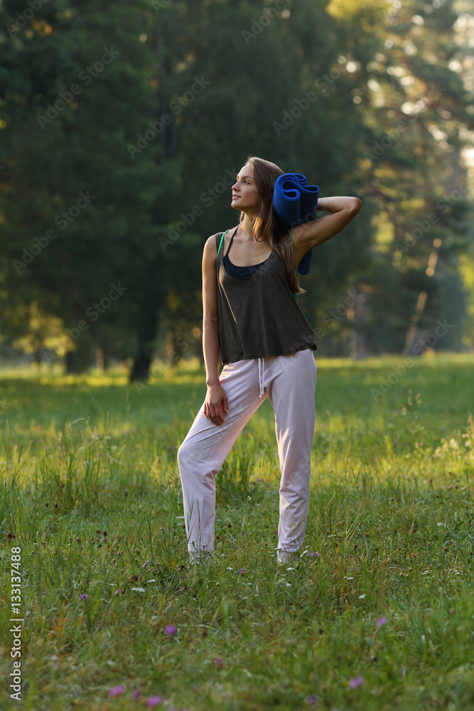 Beautiful girl looking away and holding yoga mat in park Beautiful girl looking away and holding yoga mat in park