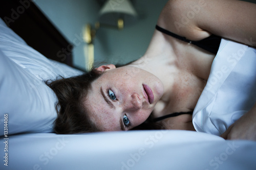 Portrait of pensive and sad woman in bed with green eyes
