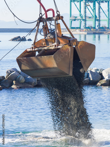 Dredge Clamshell Bucket unloading gravel in the water of a port next to the shore to replenish a beach 
 photo