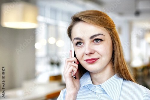 Beautiful young girl speaks on a cell phone in a light office room