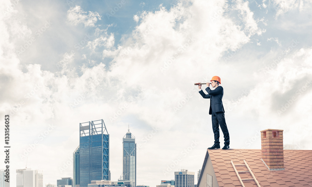 Engineer man standing on roof and looking in spyglass. Mixed med